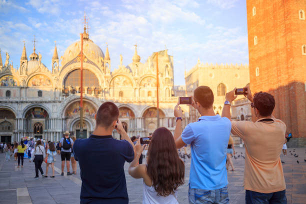 turisti a venezia. giovani donne e giovani uomini, divertitevi. gruppo di amici che scattano una foto con lo smartphone, cattedrale di san marco in piazza san marco, venezia. stili di vita casual scena urbana italia.  visitare venezia, italia. - photography urban scene venice italy veneto foto e immagini stock