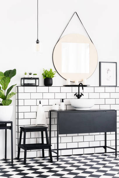 istock Plants and mirror in black and white bathroom interior with checkered floor and stool. Real photo 1002701592