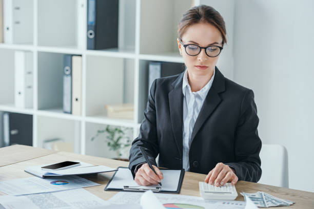 istock attractive financier working at table in office with calculator and clipboard 1002705162
