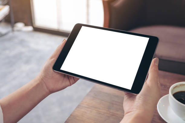 istock Mockup image of a woman's hands holding black tablet pc with white blank screen with coffee cup on table 1002705960