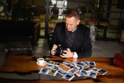 Senior male photographer examining some images. Various photographs and DSLR camera are on the table.
