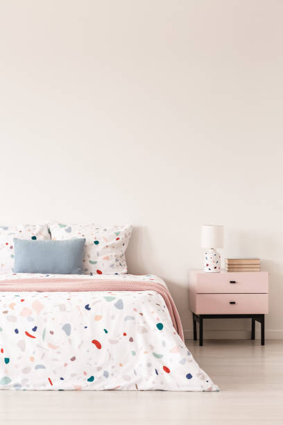 istock Lamp on cabinet next to patterned bed with blue pillow and pink blanket in bedroom interior. Real photo 1002720176