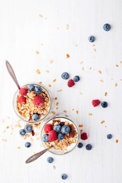 Granola with berries and yogurt in jars. Two jars with granola, berries and yogurt on white wooden table. Top view. yogurt parfait stock pictures, royalty-free photos & images