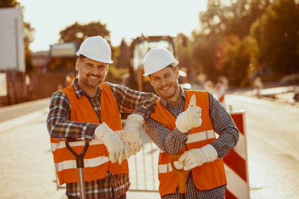 Two construction workers in hardhats and vests posing for a photo at the road