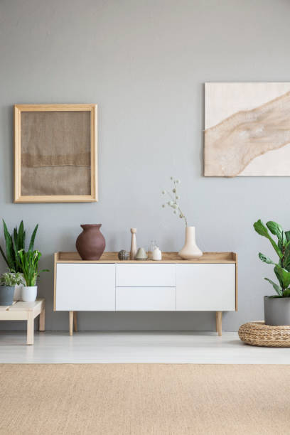 istock White cupboard between plants in grey living room interior with posters and brown carpet. Real photo 1002732284