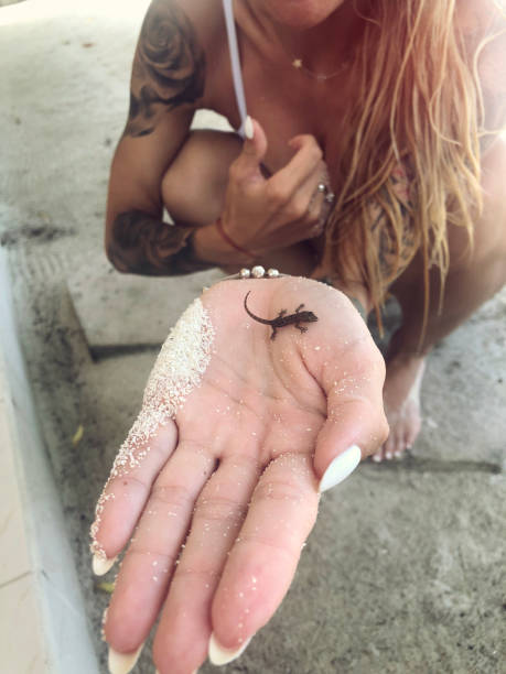 Tattooed woman holding little lizard in hand on the beach on Maldives.