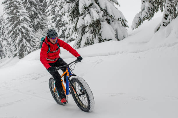 istock Man fat biking on snowy trail through winter forest 1002736034