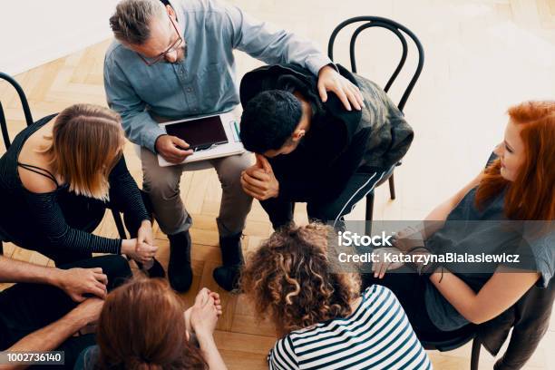 Unterstützende Therapeut Beruhigend Einen Jungen Mann Der Seine Eltern In Der Gruppe Therapie Für Menschen In Trauer Verloren Stockfoto und mehr Bilder von Psychosoziale Beratung