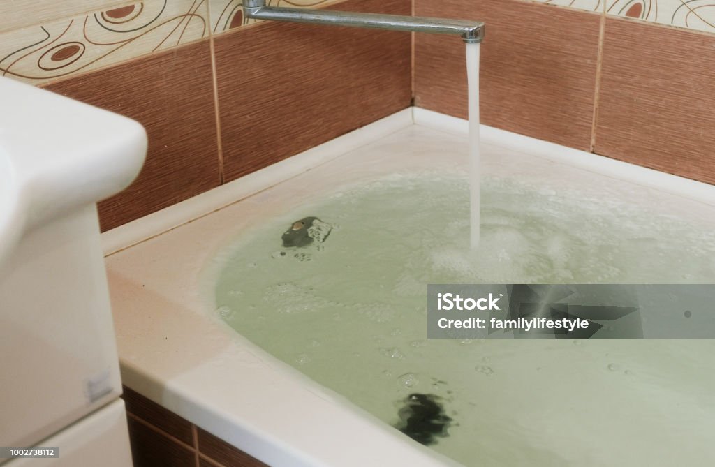 Strong stream of water pours into the tub. Water pours out. Tub overflows. Close up. Strong stream of water pours into the tub. Water pours out. Tub overflows. Close up Bathtub Stock Photo