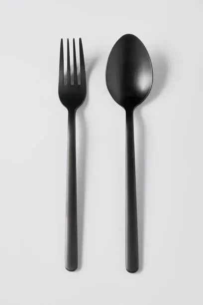 Photo of top view of black fork and spoon on white background, minimalistic concept