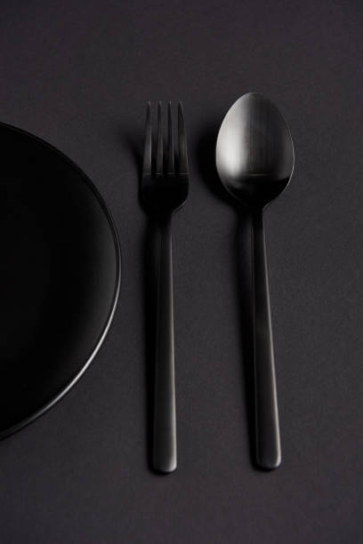 istock top view of black spoon, fork and plate on black table, minimalistic concept 1002740872