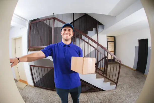 Young postal worker delivering package to your door is ringing a doorbell.