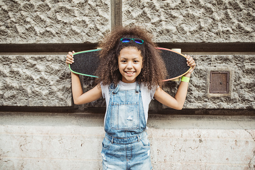 Girl on street enjoy in beautiful day and have fun on longboard. She holding longboard on shoulders and smiling