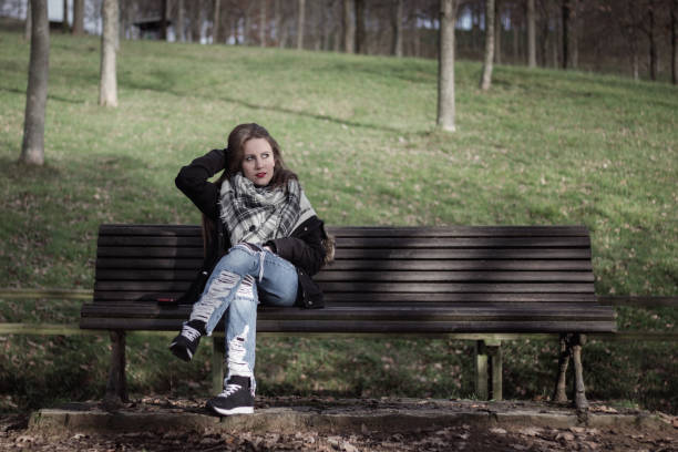 istock Young woman sitting on park bench adjusts her hair while looking at sunlight 1002752574