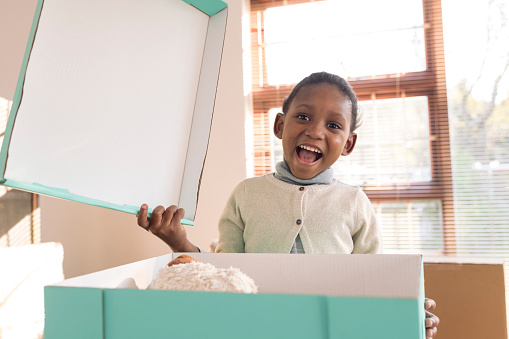 Little girl opens moving box of toys smiling at camera