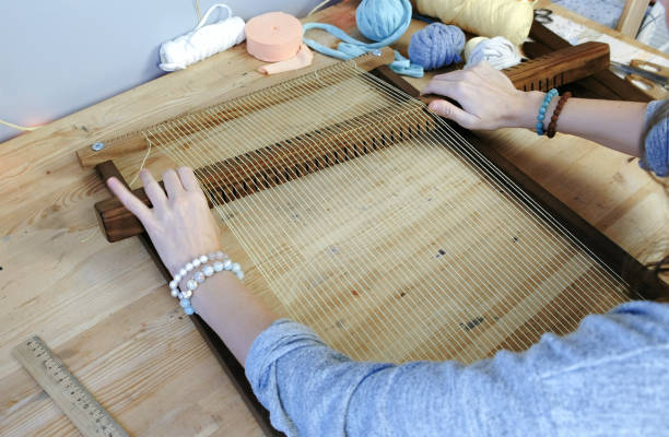 istock Weaving on a loom frame. Closeup woman's hand puts the thread in the frame for weaving. 1002768570