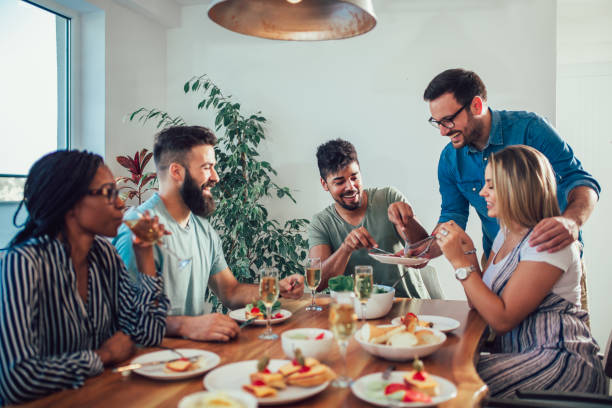 istock Group Of Happy Young Friends Enjoying Dinner At Home. 1002771920