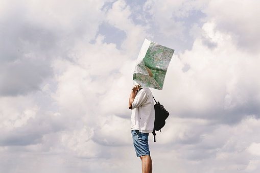 hipster traveler on top of mountains with amazing sky clouds view and map at his head, funny moment,  travel adventure and gps concept, space for text