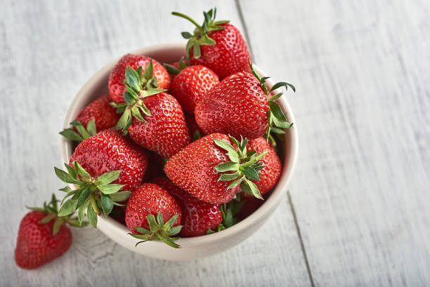 istock Fresh strawberries in ceramic bowl on rustic white wooden background. 1002783242