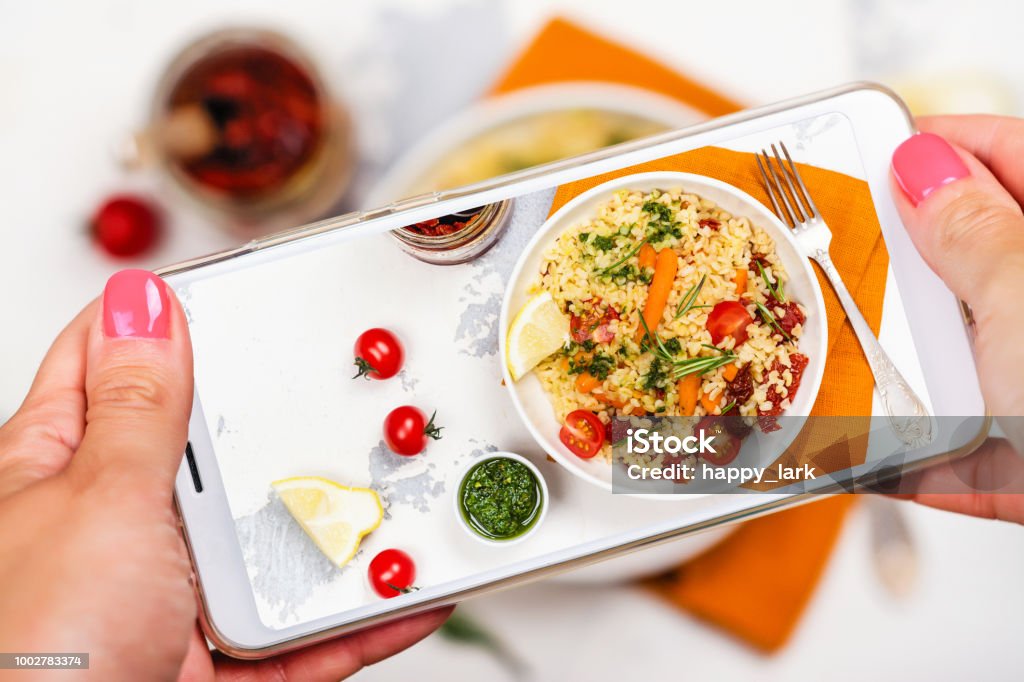 Smartphone photo of bulgur salad Female hands with smart phone taking photo of bulgur salad. Mobile shot food photo Auto Post Production Filter Stock Photo