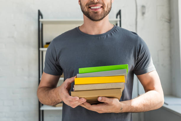 istock cropped image of smiling man standing with stack of books at home 1002792510
