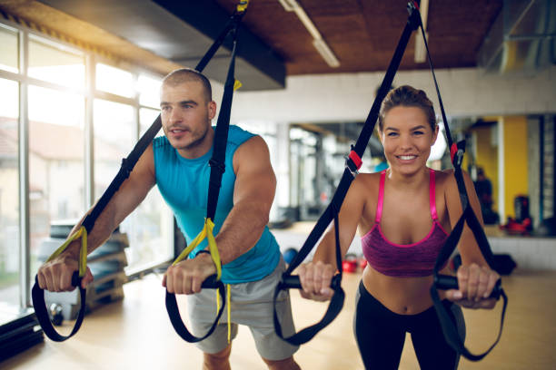 istock Couple doing arm exercises with suspension straps at gym 1002792676