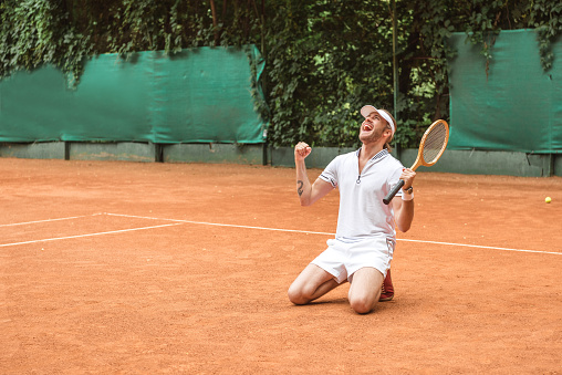 blond winner with racket celebrating and kneeling on tennis court