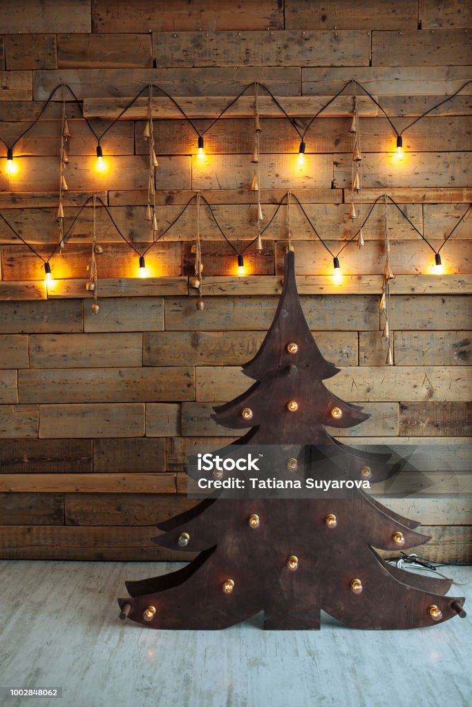 Alternative wooden christmas tree. A handmade New Year tree with light bulb on the floor on wooden background. Loft interior. Copy space Alternative wooden christmas tree. A handmade New Year tree with light bulb on the floor on wooden background. Loft interior. Copy space. Alternative Lifestyle Stock Photo