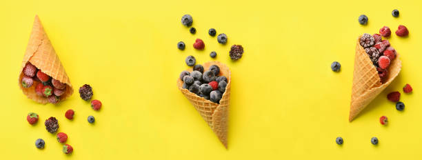 Frozen berries - strawberry, blueberry, blackberry, raspberry in waffle cones on yellow background. Top view. Banner. Pattern for minimal style. Pop art design, creative concept