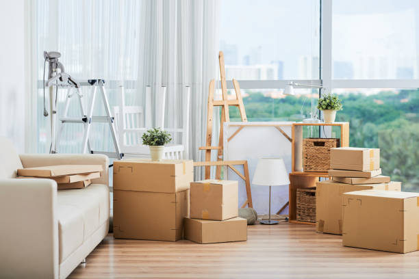 Cardboard boxes for moving and drawing easels Spacious interior with large packed carton boxed for moving on floor with sofa and drawing easels nearby at large glass wall on sunny day tidy room stock pictures, royalty-free photos & images