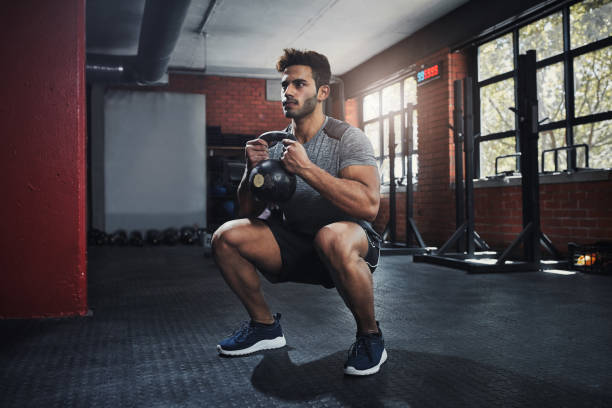 Mindset is everything Shot of a handsome young man working out at the gym crouching stock pictures, royalty-free photos & images