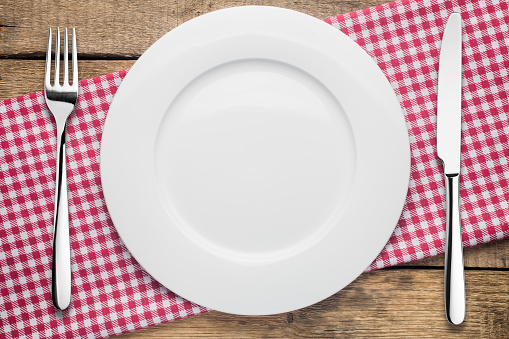 empty plate on a wooden background, a napkin in a red and white cage, a fork a knife