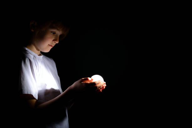 Cute little girl holding a luminous led light bulb in the dark stock photo
