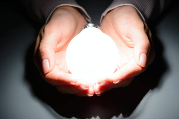 istock Female hands holding a glowing led bulb in the dark 1002864676