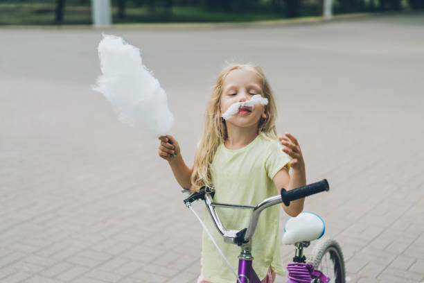 portrait of little child with bicycle having fun and making mustache from cotton candy on street portrait of little child with bicycle having fun and making mustache from cotton candy on street child cotton candy stock pictures, royalty-free photos & images