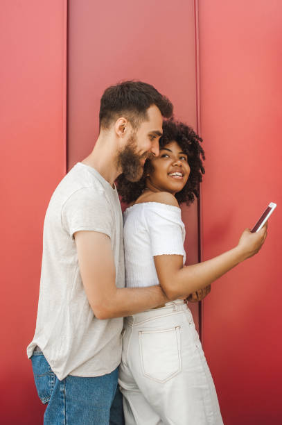 istock handsome young man hugging smiling girlfriend using smartphone on street 1002874014