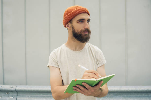 handsome bearded man writing in notebook and looking away on street