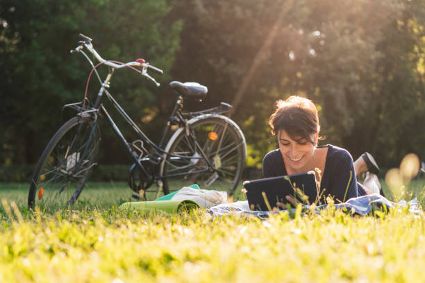 junge frau ein ebook in einem öffentlichen park lesen - short cycle stock-fotos und bilder