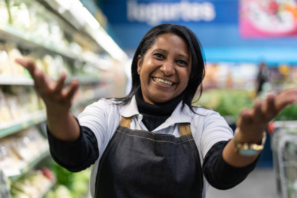 supermarket employee woman beckoning - inviting clients to come - beckoning imagens e fotografias de stock