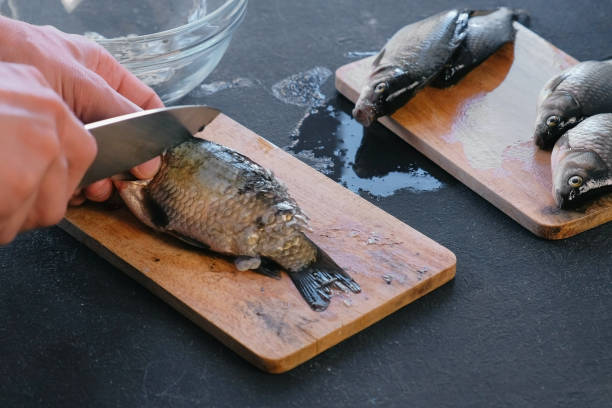 istock Man cleans carp from the scales. Close-up hands. Cooking a fish. 1002887864