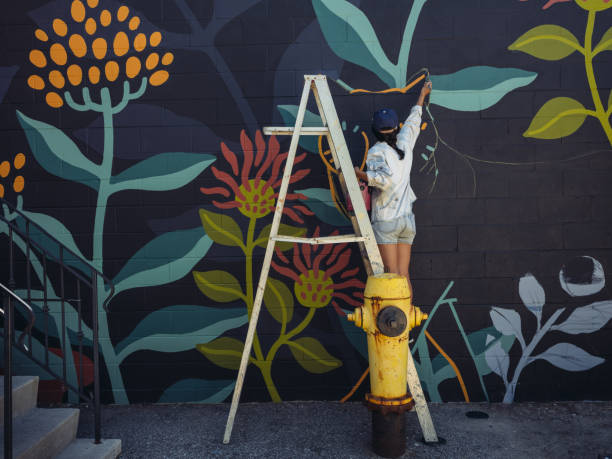 Mural artist at work Young Asian woman, mural artist creating wall art at the urban setting. street art mural stock pictures, royalty-free photos & images