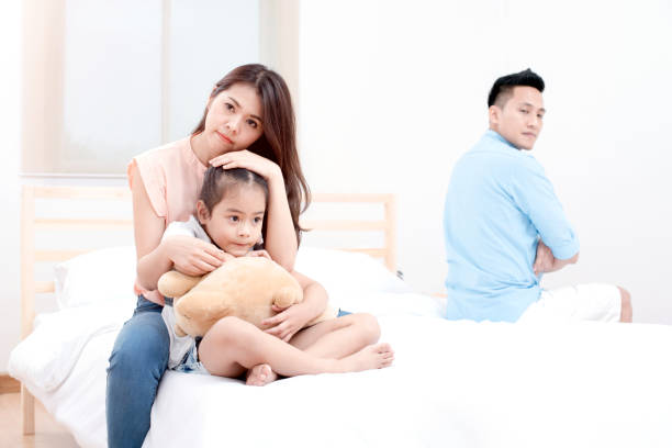 a little girl sad with her parents are arguing in the background bed room, Asian happy loving family.Soft and select focus. stock photo