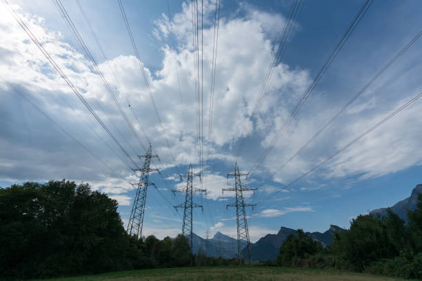 istock power lines and pylons in silhouette against a blue sky with white clouds and trees below 1002940288