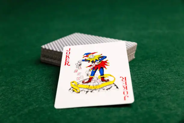 Close-up of a red Joker leaning against a face-down deck of cards on a green baize background