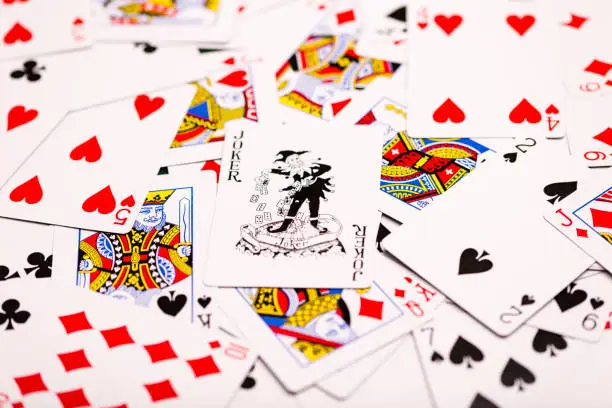 A pack of playing-cards spread out across the table with a black Joker central