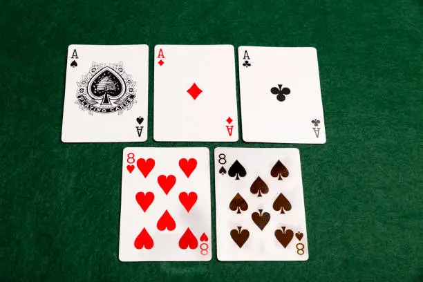 A full house of three aces and two eights laid out on a green baize background