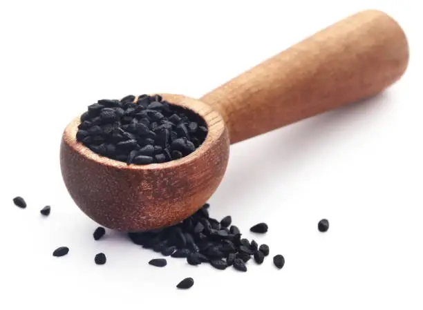 Nigella seeds in wooden scoop over white background