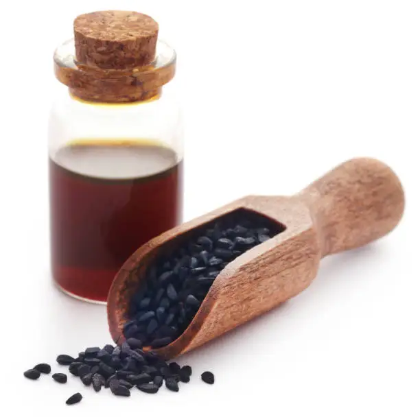 Nigella seeds and essential oil in a glass bottle over white background