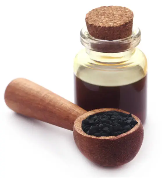 Nigella seeds and essential oil in a glass bottle over white background