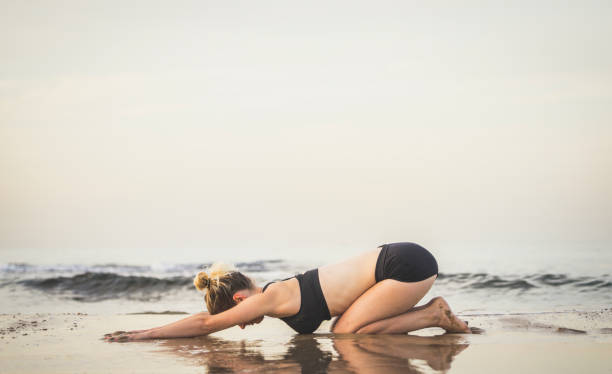 Young Woman Practicing Child Pose Yoga Pose On The Beach stock photo